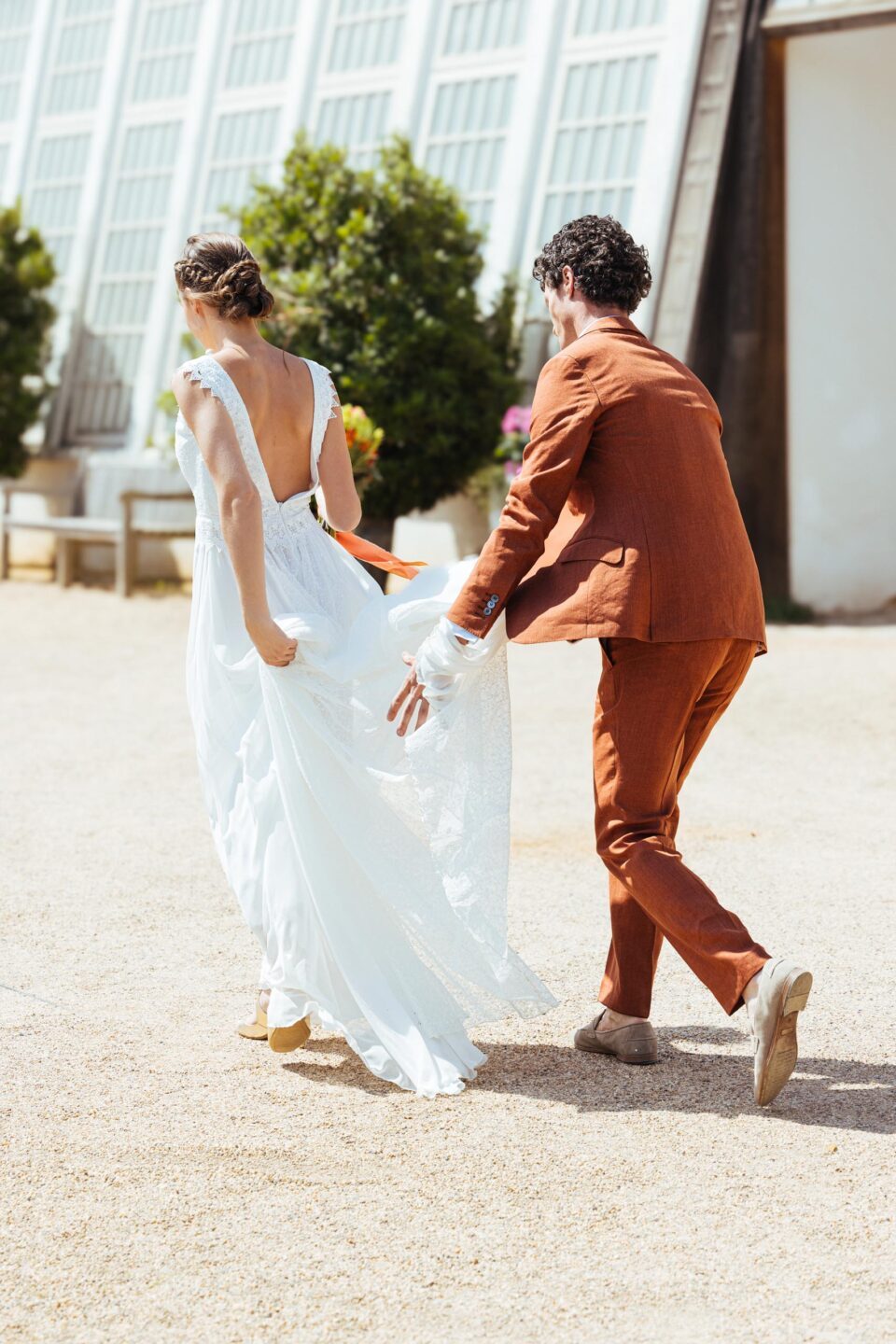 Braut im rückenfreien Hochzeitskleid wird die Schleppe vom Bräutigam gehalten