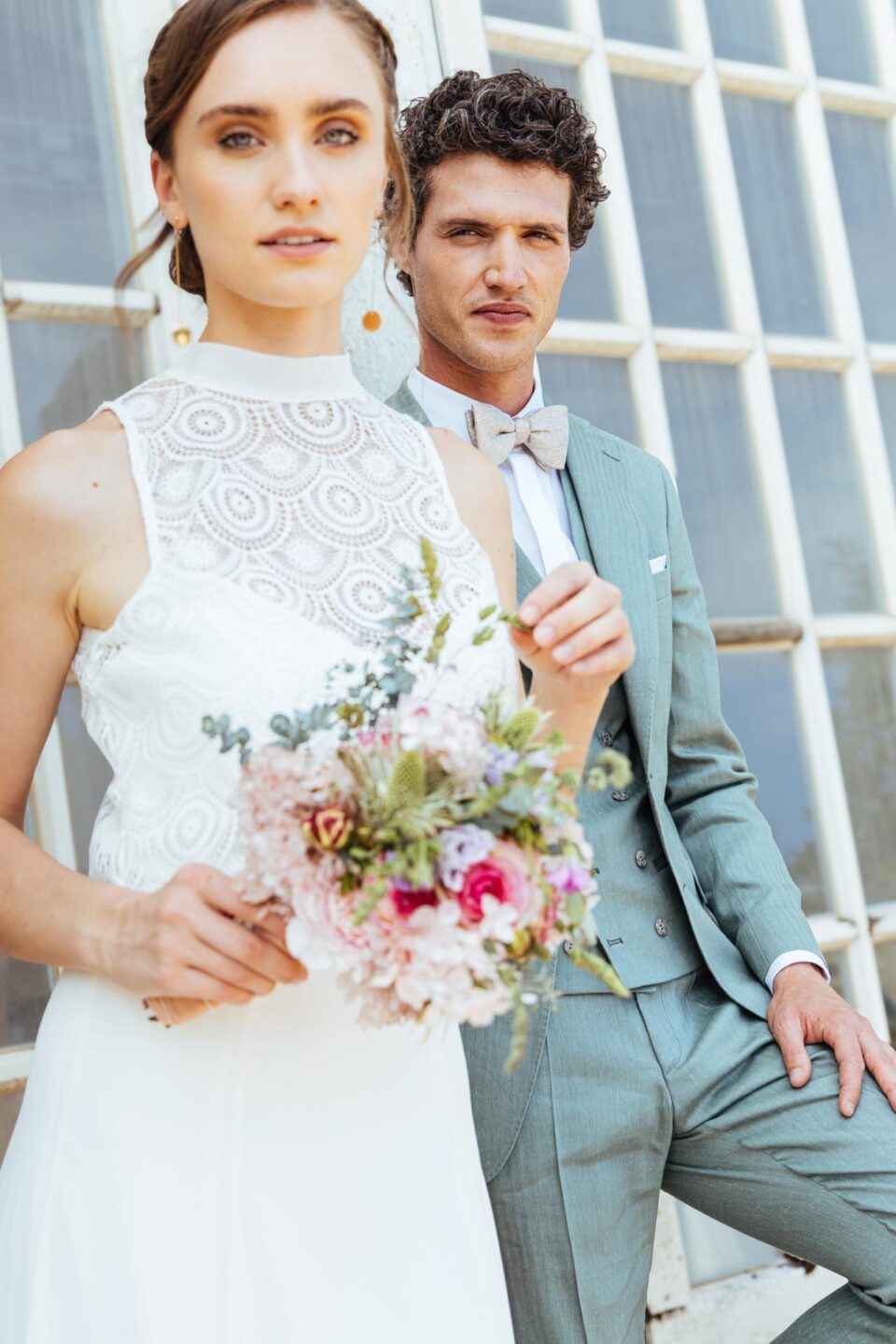 Braut in Brautkleid mit Stehkragen im Vordergrund, Bräutigam im Hintergrunde.